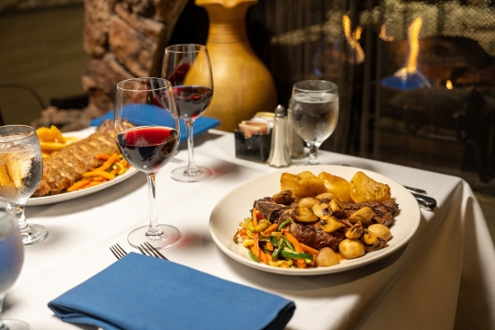 Grilled steak topped with mushrooms, roasted potatoes and vegetables, served with red wine.